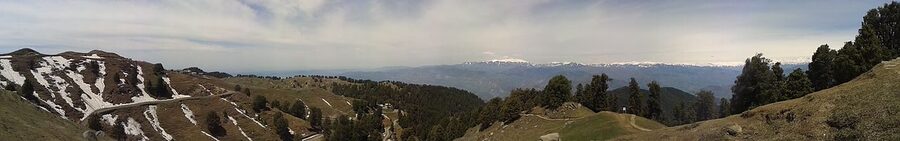 Panoramic view from Dainkund Peak showing snow-capped mountains, deodar forest and valleys below.