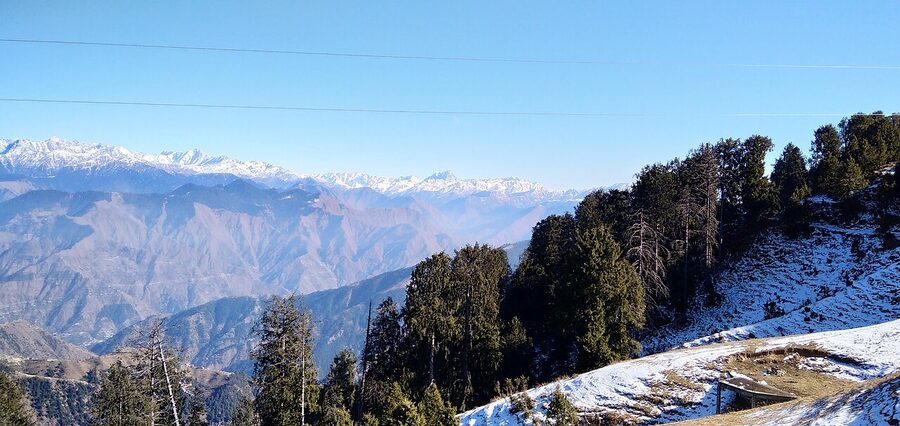 The summit of Dainkund Peak in Dalhousie with prayer flags and panoramic Himalayan views.