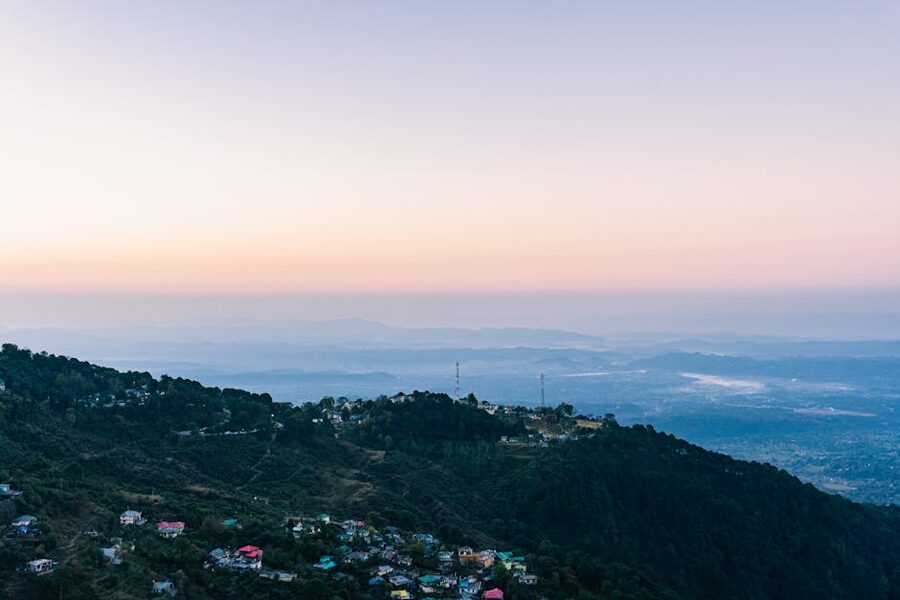 Aerial sunset view of Dalhousie hills with red-roofed buildings and forested ridges glowing in evening light.