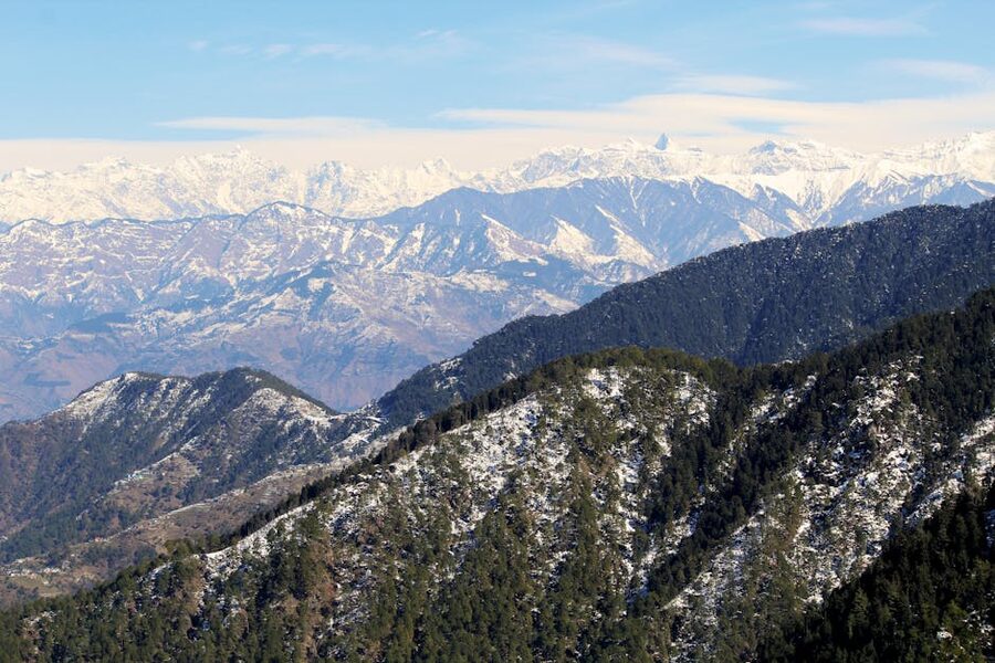 Snow-covered slopes and trees in Dalhousie during winter with mountain peaks in the distance.