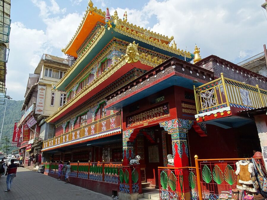 The main street temple area in McLeod Ganj with prayer flags, shops, and pedestrians, Himachal Pradesh.