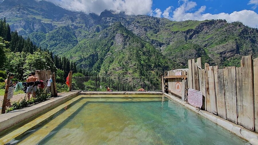 The Kheerganga hot spring pool in the meadow with mist rising from the water.