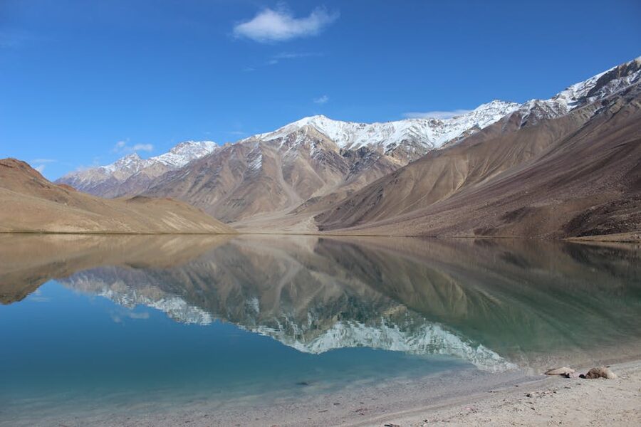 Chandra Taal lake reflecting the snow-capped Himalayan range under a clear sky.