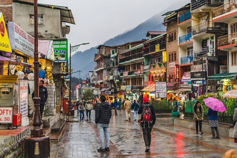 Mall Road in central Manali on a clear afternoon, the main pedestrian street lined with shops