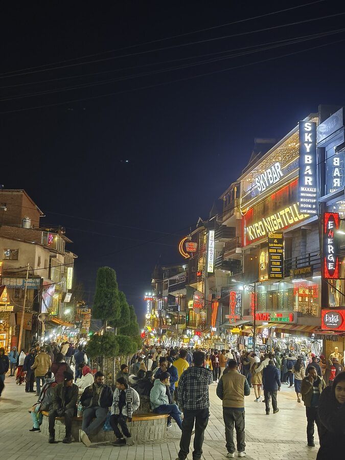 Mall Road in central Manali with shops and the Durga Mata temple visible.