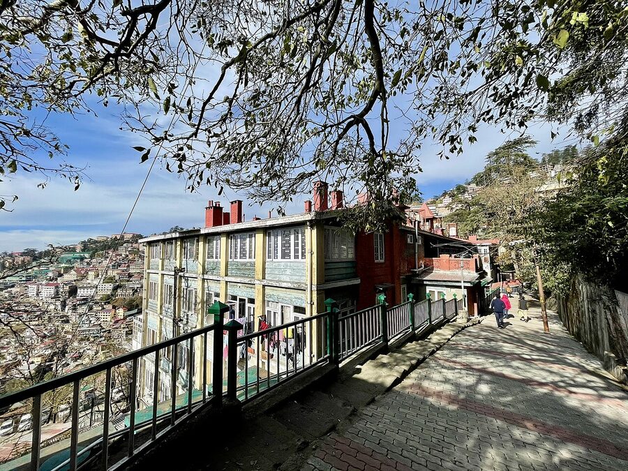 A street-level view of Mall Road in Shimla with shops, cafes, and the Town Hall in the distance.