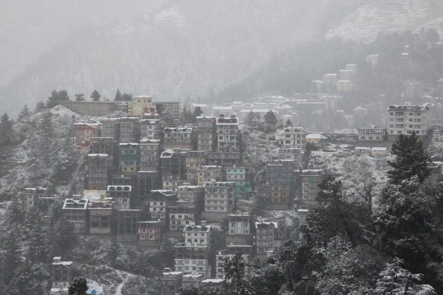 Snow-covered rooftops and buildings in Shimla under winter cloud cover.
